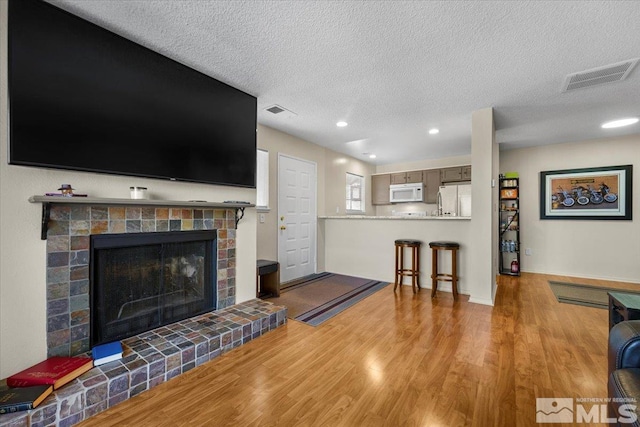 living room with a textured ceiling, light wood-type flooring, and a tile fireplace