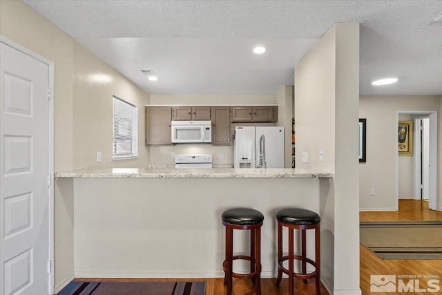 kitchen featuring a textured ceiling, kitchen peninsula, a breakfast bar, and white appliances