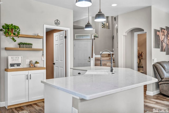 kitchen featuring decorative light fixtures, hardwood / wood-style floors, light stone countertops, an island with sink, and white cabinets