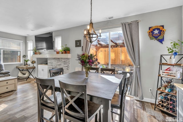 dining area with light wood-type flooring, a chandelier, and a stone fireplace