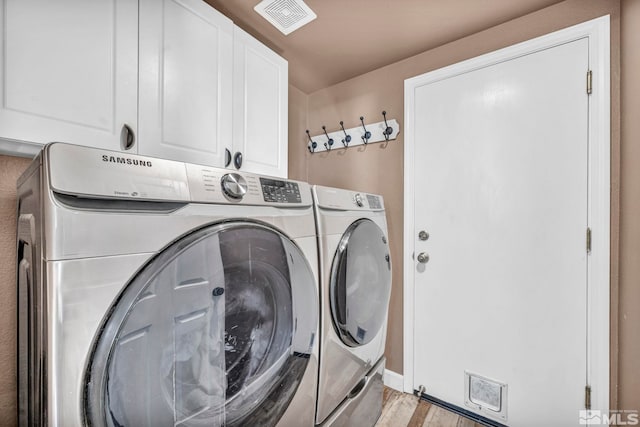 laundry room featuring cabinets, washer and clothes dryer, and light hardwood / wood-style flooring