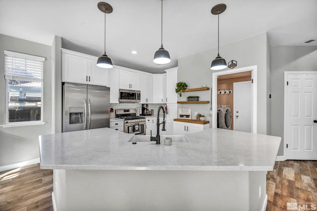 kitchen featuring white cabinetry, stainless steel appliances, washer and dryer, decorative light fixtures, and sink