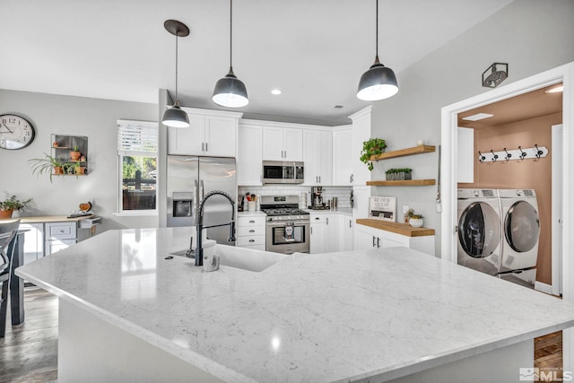 kitchen with washer and dryer, sink, hanging light fixtures, light stone countertops, and stainless steel appliances