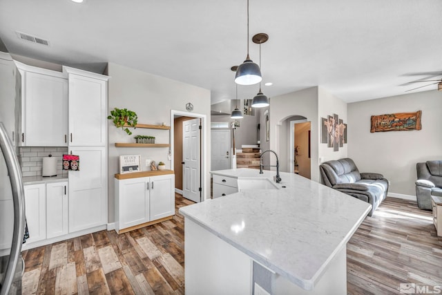 kitchen featuring white cabinetry, a center island with sink, hanging light fixtures, light stone counters, and sink