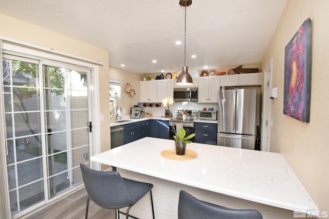 kitchen with a kitchen bar, stainless steel appliances, hanging light fixtures, white cabinets, and sink