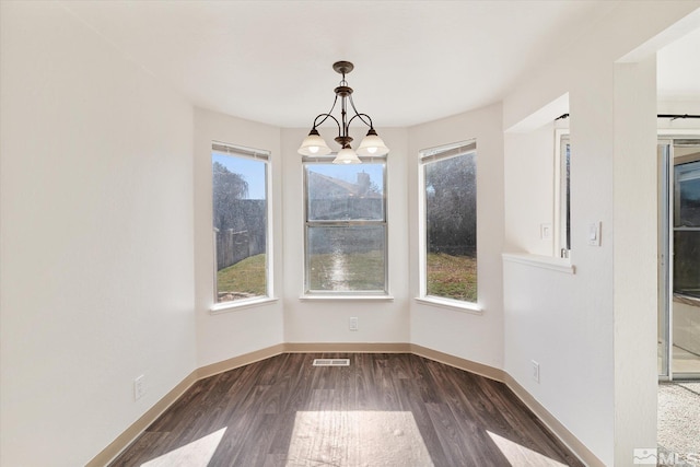 unfurnished dining area with dark wood-type flooring and an inviting chandelier