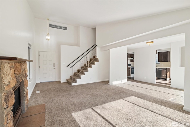 unfurnished living room featuring a towering ceiling, carpet, and a stone fireplace