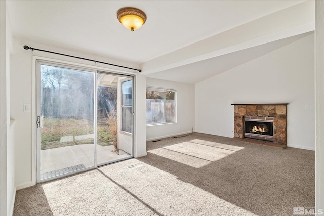 unfurnished living room with a wealth of natural light, carpet flooring, a stone fireplace, and vaulted ceiling