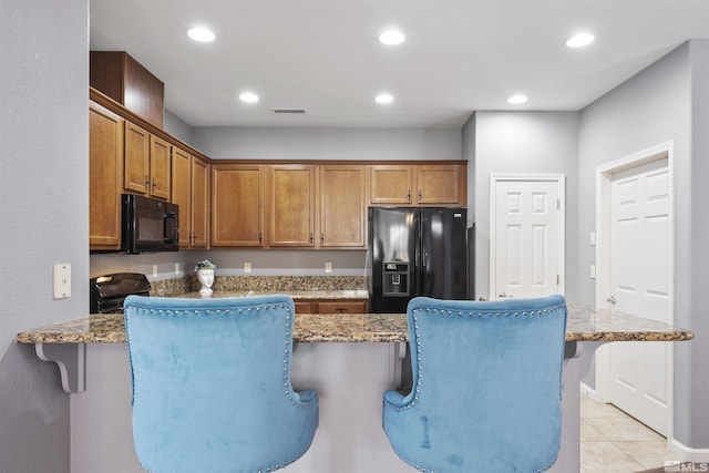 kitchen with light tile patterned floors, kitchen peninsula, a kitchen breakfast bar, stone countertops, and black appliances