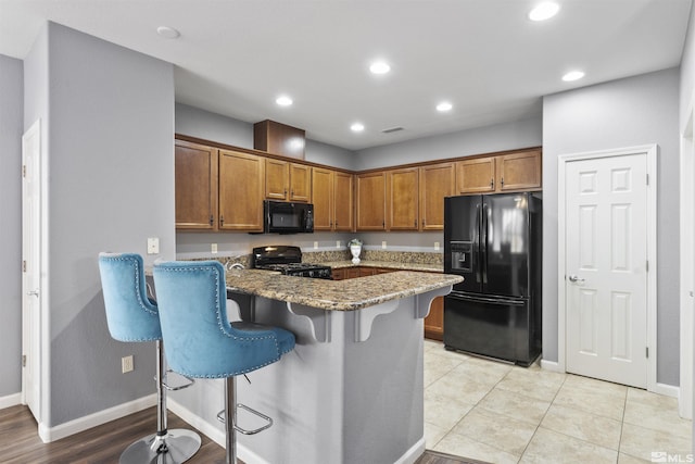 kitchen featuring black appliances, kitchen peninsula, a kitchen breakfast bar, light tile patterned floors, and stone countertops