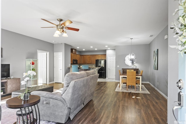 living room with dark wood-type flooring and ceiling fan with notable chandelier