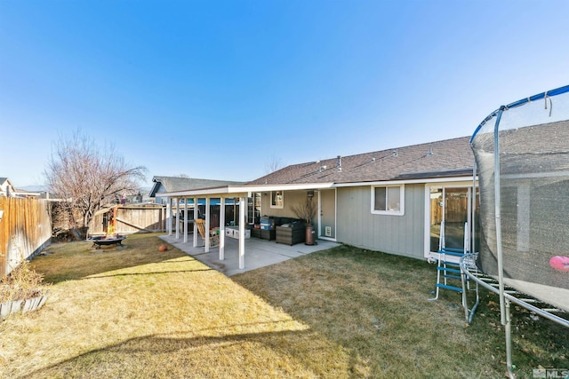 rear view of property with a trampoline, a yard, and a patio