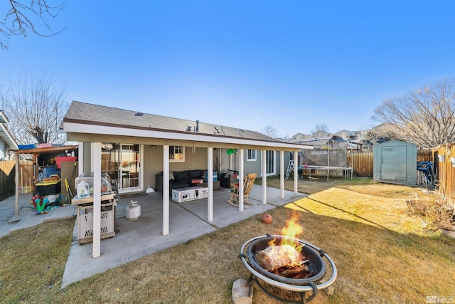 rear view of property with a patio, a lawn, a trampoline, an outdoor fire pit, and a storage shed