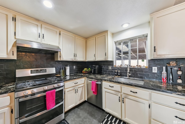 kitchen with sink, tasteful backsplash, appliances with stainless steel finishes, dark tile patterned floors, and dark stone counters