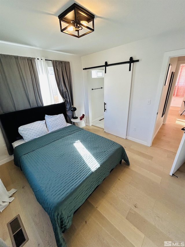 bedroom with a barn door, connected bathroom, and hardwood / wood-style flooring