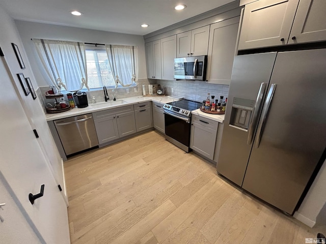 kitchen featuring decorative backsplash, sink, light wood-type flooring, gray cabinetry, and stainless steel appliances