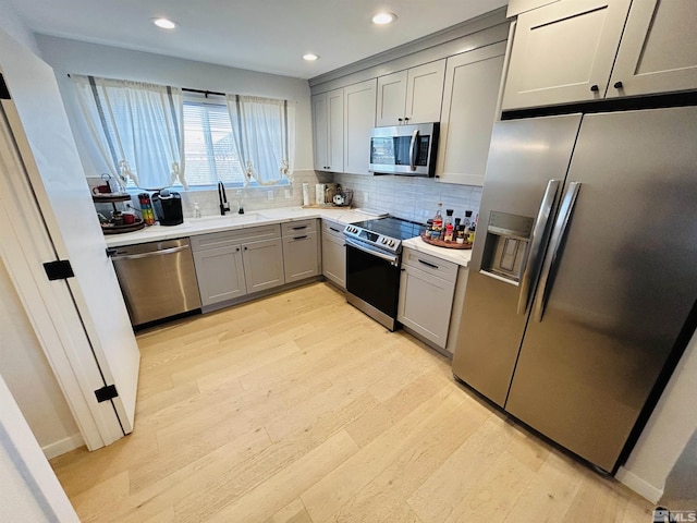 kitchen with appliances with stainless steel finishes, light hardwood / wood-style floors, sink, backsplash, and gray cabinetry