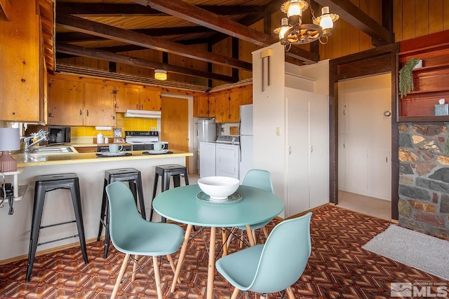 kitchen with a notable chandelier, beam ceiling, kitchen peninsula, sink, and high vaulted ceiling