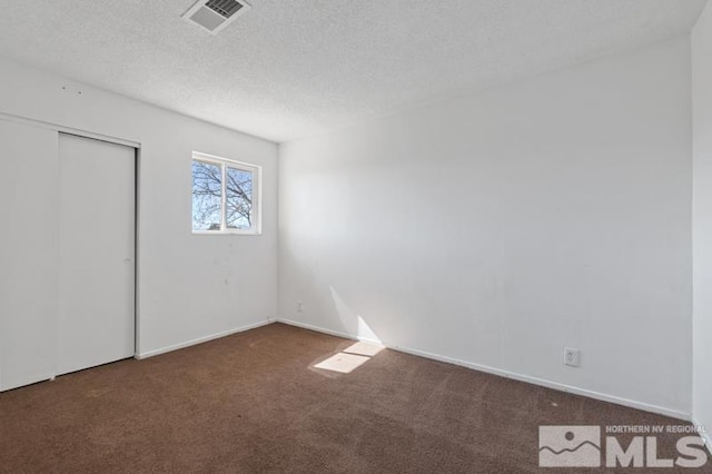 unfurnished bedroom with a textured ceiling, visible vents, baseboards, a closet, and carpet