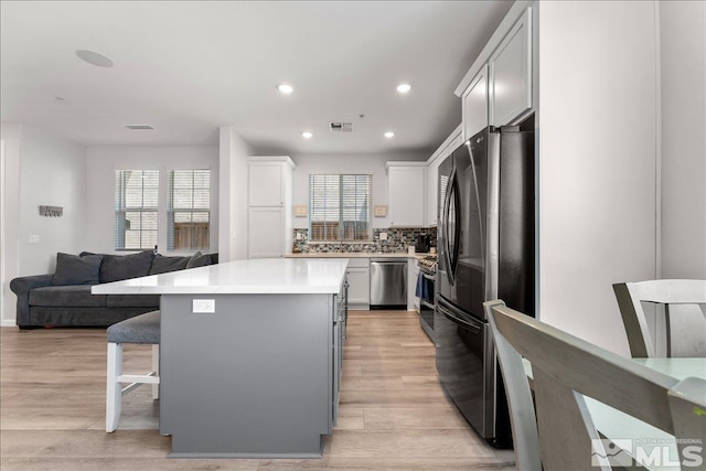 kitchen featuring refrigerator, light hardwood / wood-style floors, stainless steel dishwasher, a center island, and decorative backsplash