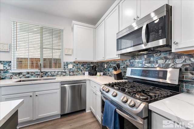 kitchen featuring light stone countertops, appliances with stainless steel finishes, white cabinetry, sink, and light hardwood / wood-style flooring