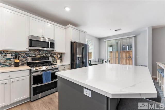 kitchen featuring white cabinets, appliances with stainless steel finishes, a center island, backsplash, and light stone counters