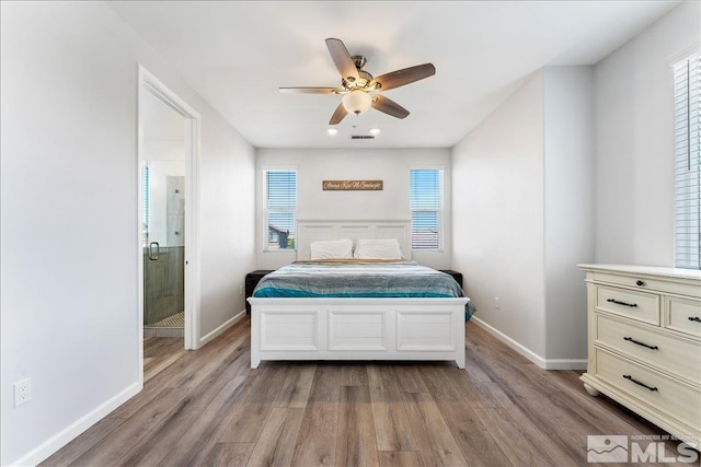 bedroom featuring ceiling fan, multiple windows, ensuite bath, and light wood-type flooring