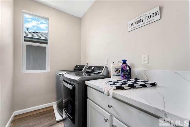 clothes washing area featuring cabinets, washer and clothes dryer, and light hardwood / wood-style flooring