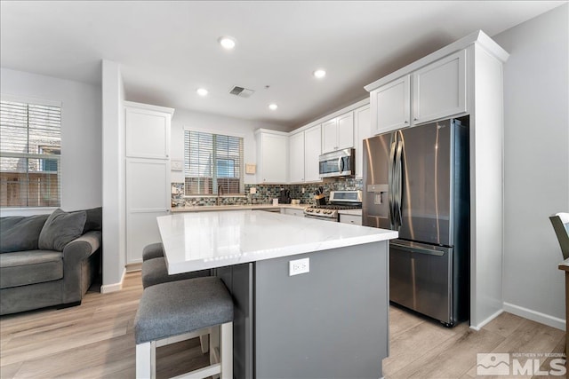 kitchen featuring light hardwood / wood-style floors, appliances with stainless steel finishes, tasteful backsplash, a kitchen island, and white cabinets