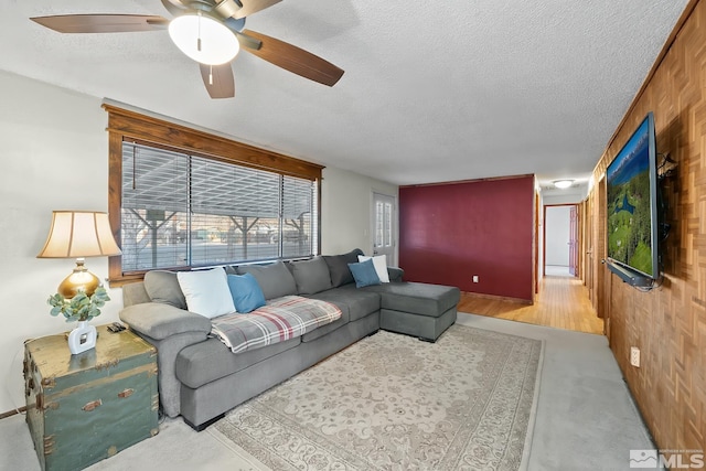 carpeted living room featuring ceiling fan, wooden walls, and a textured ceiling