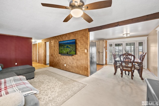 living room featuring ceiling fan, a textured ceiling, and beamed ceiling