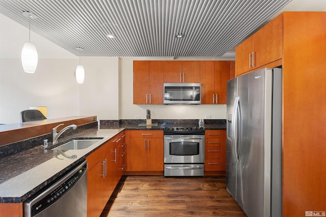 kitchen featuring pendant lighting, kitchen peninsula, sink, appliances with stainless steel finishes, and dark stone counters