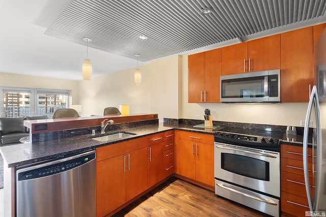 kitchen featuring dark stone countertops, kitchen peninsula, sink, hanging light fixtures, and stainless steel appliances