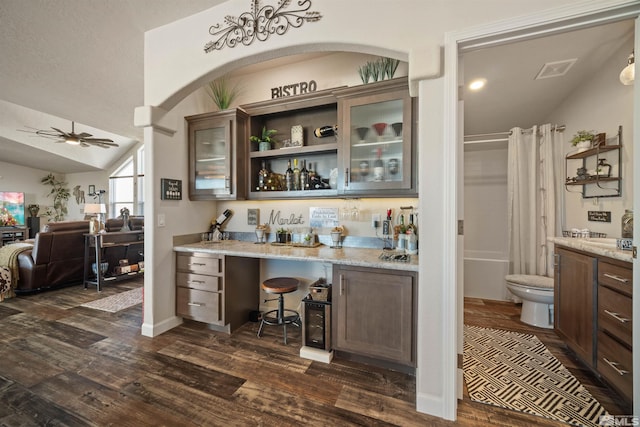 bar featuring ceiling fan, dark hardwood / wood-style flooring, light stone counters, and dark brown cabinetry