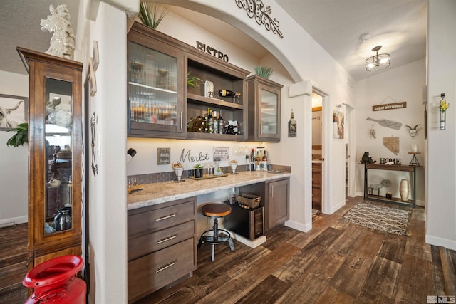 bar with dark wood-type flooring, light stone counters, and dark brown cabinets