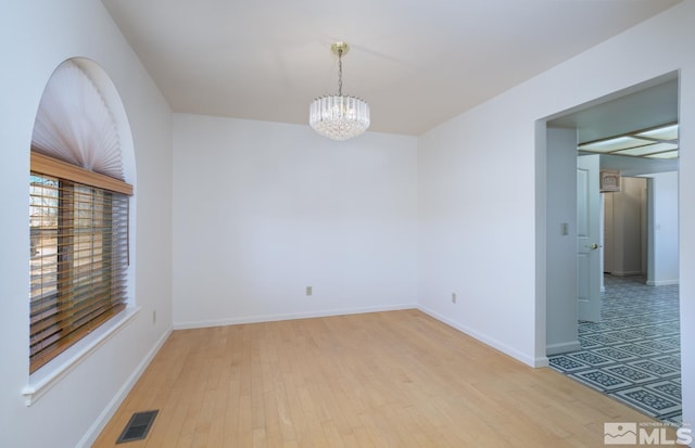 empty room featuring light wood-type flooring and a notable chandelier