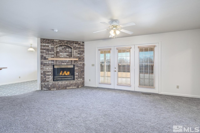 unfurnished living room featuring a brick fireplace, french doors, ceiling fan, and carpet flooring