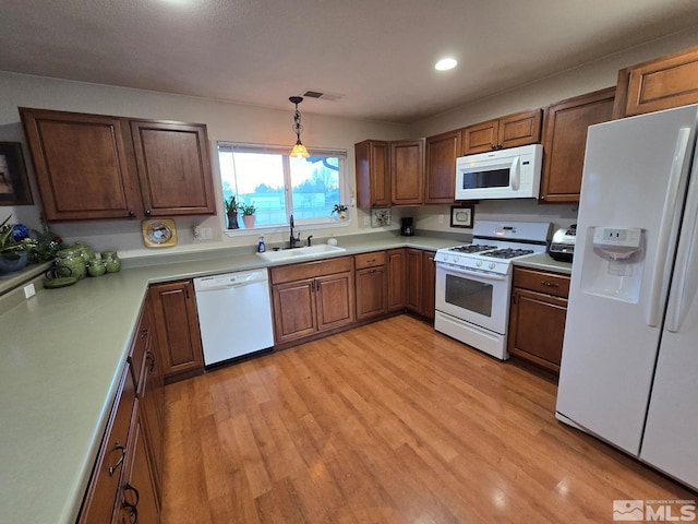 kitchen with sink, white appliances, decorative light fixtures, and light hardwood / wood-style floors