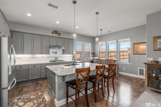 kitchen with a center island with sink, stainless steel appliances, decorative light fixtures, light stone countertops, and sink