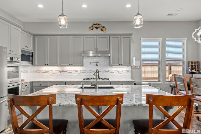 kitchen with a kitchen bar, appliances with stainless steel finishes, gray cabinets, and pendant lighting