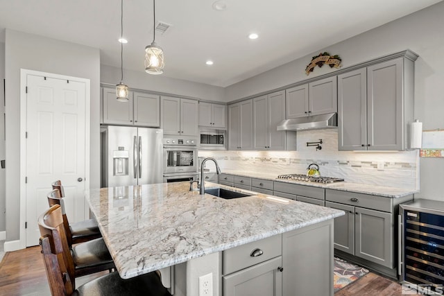 kitchen with wine cooler, a kitchen island with sink, appliances with stainless steel finishes, and sink