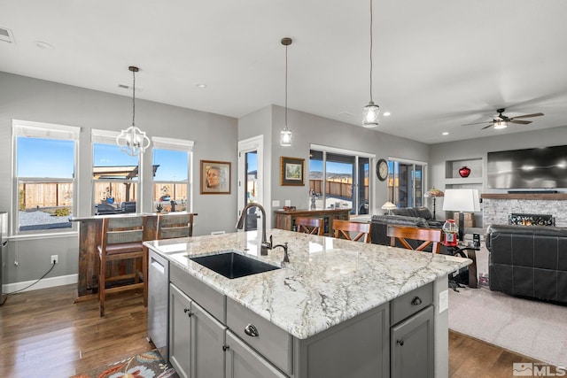 kitchen with light stone counters, sink, pendant lighting, and a center island with sink