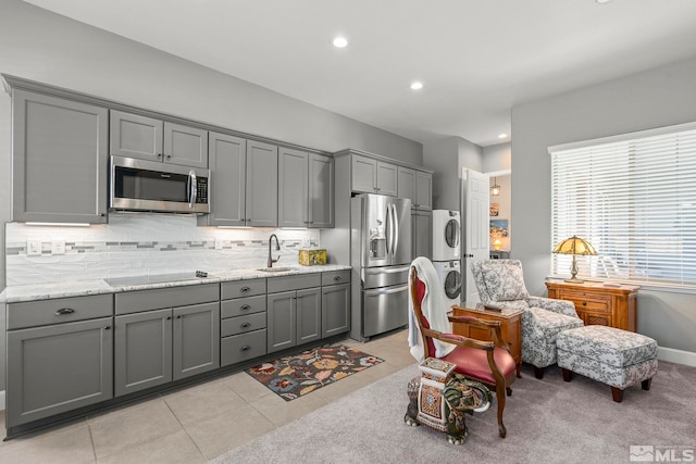 kitchen featuring sink, stacked washer / dryer, gray cabinetry, stainless steel appliances, and light stone counters