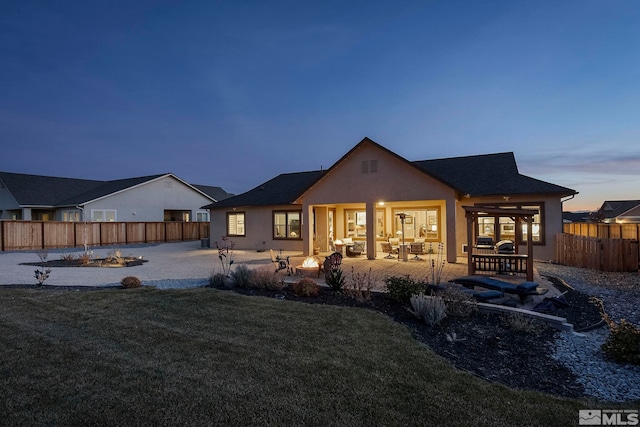 back house at dusk with a lawn, a fire pit, and a patio