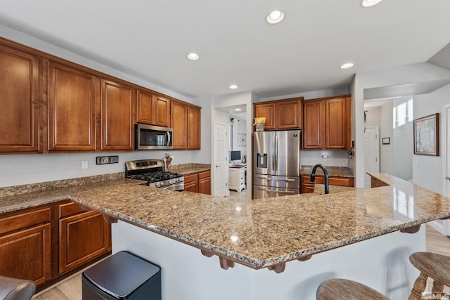 kitchen with a kitchen bar, light stone countertops, appliances with stainless steel finishes, and an island with sink