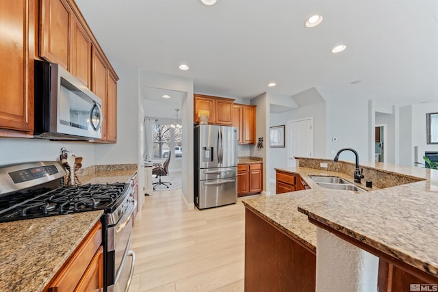 kitchen with light stone countertops, appliances with stainless steel finishes, an inviting chandelier, sink, and light wood-type flooring