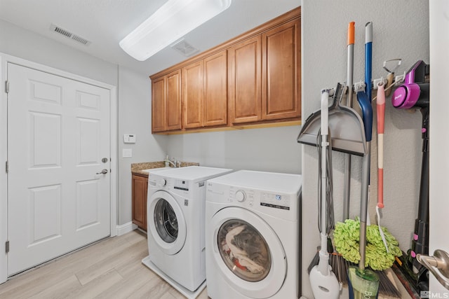 laundry room featuring cabinets, washer and clothes dryer, and light hardwood / wood-style flooring