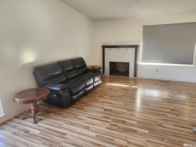 living room with a brick fireplace, a textured ceiling, and light wood-type flooring