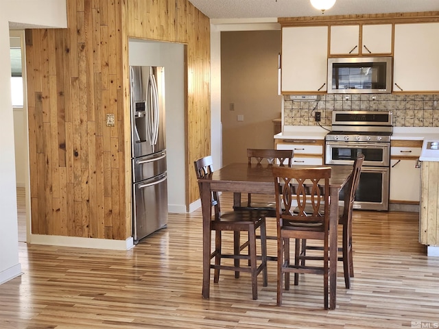 kitchen with white cabinets, light wood-type flooring, appliances with stainless steel finishes, and wood walls