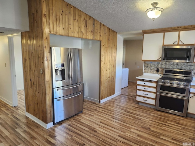 kitchen featuring a textured ceiling, white cabinetry, stainless steel appliances, wooden walls, and light hardwood / wood-style floors